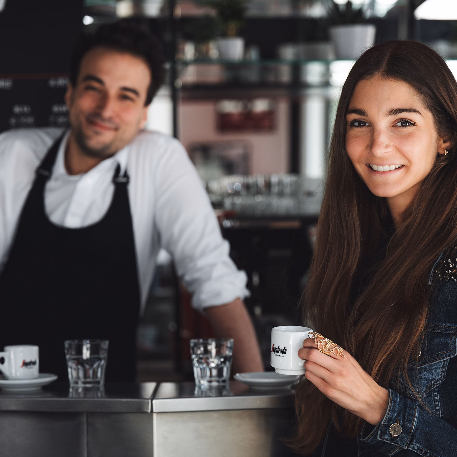 Frau mit Espressotasse vor Theke und Barista hinter der Theke