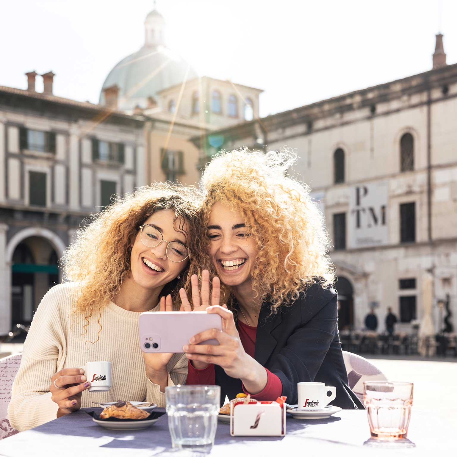 2 Frauen mit Smartphone an einem Tisch auf einem Platz